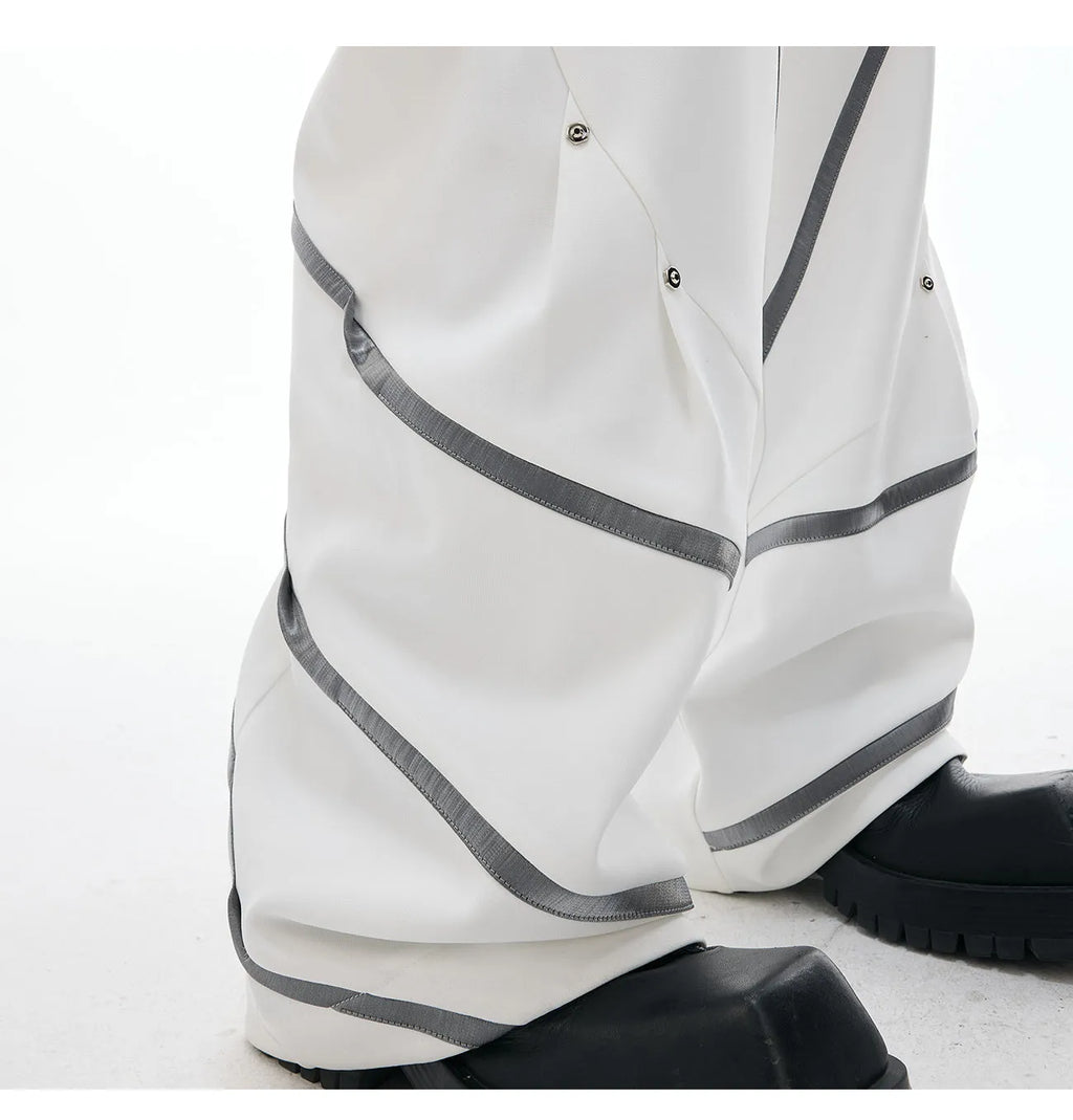 Men's black trousers with white pleated detail and silver metal striped rivets, showing the three-dimensional cut.