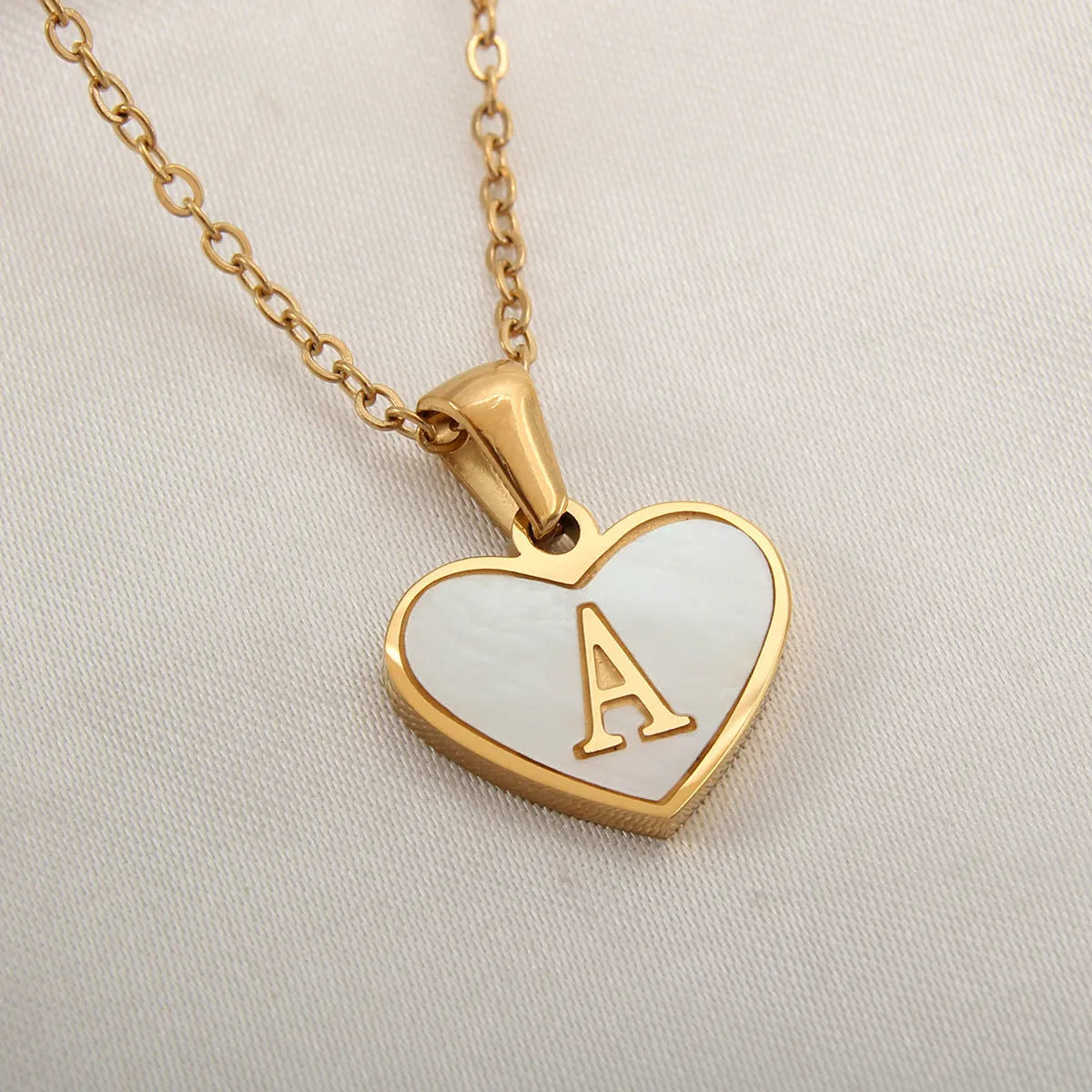 Gold-plated heart necklace with white shell pendant showing initial engraving on stainless steel chain