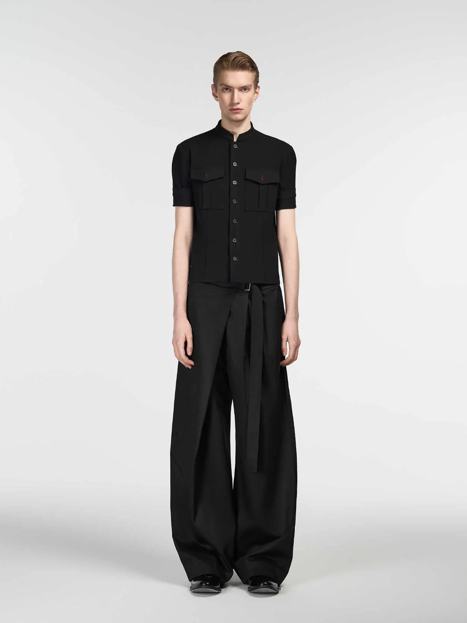Black loose fit straight leg trousers with a single pleat and adjustable waistband on a hanger.