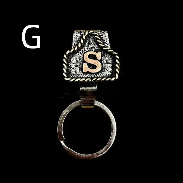 Handmade metal cow tag belt keychain showing one of 26 colour options, each marked with a different alphabet letter.