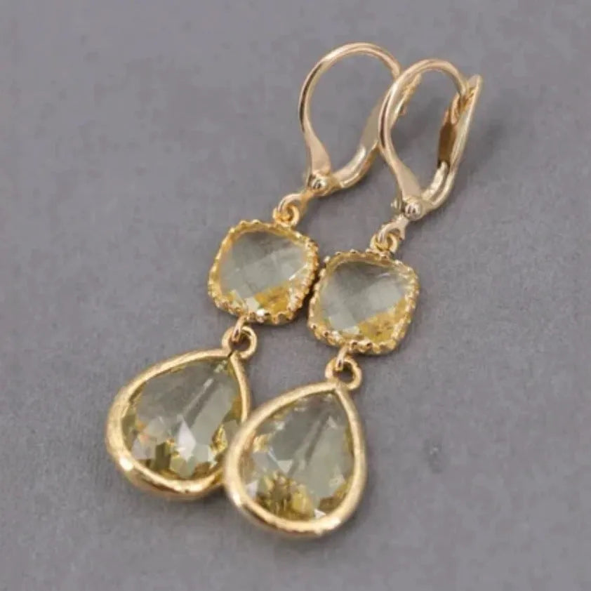 Gold geometric long fringe drop earrings with crystal and water droplet details on a white background.