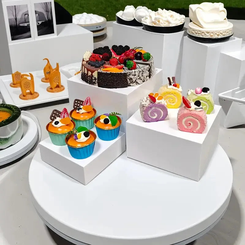 Six white plastic cube dessert display stands arranged on a table.