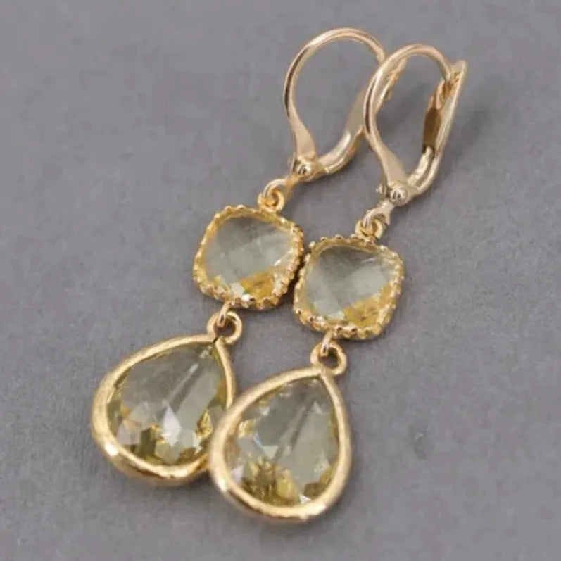 Gold geometric long fringe drop earrings with crystal and water droplet details on a white background.