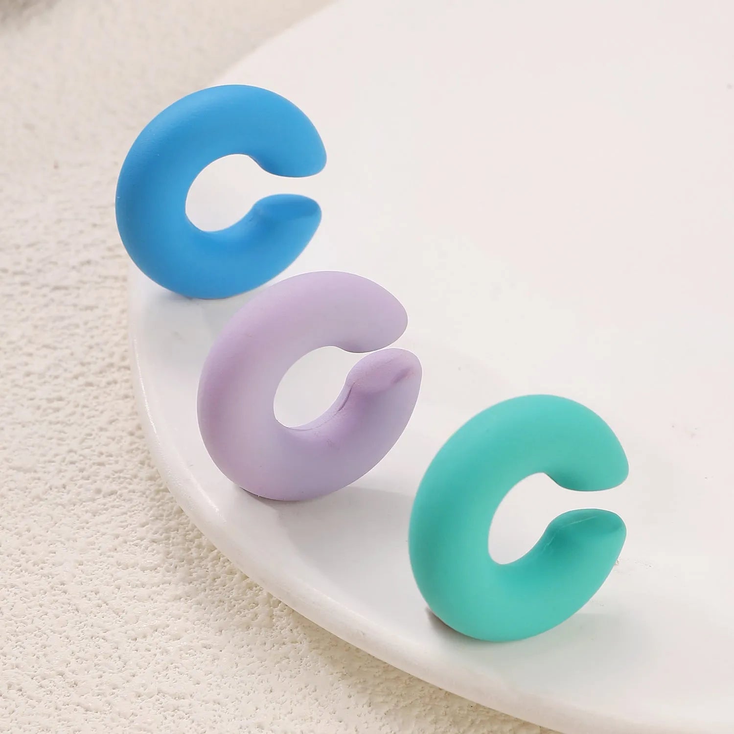 A pair of matte coarse finish round C-shaped clip-on earrings for women, shown in a candy colour.