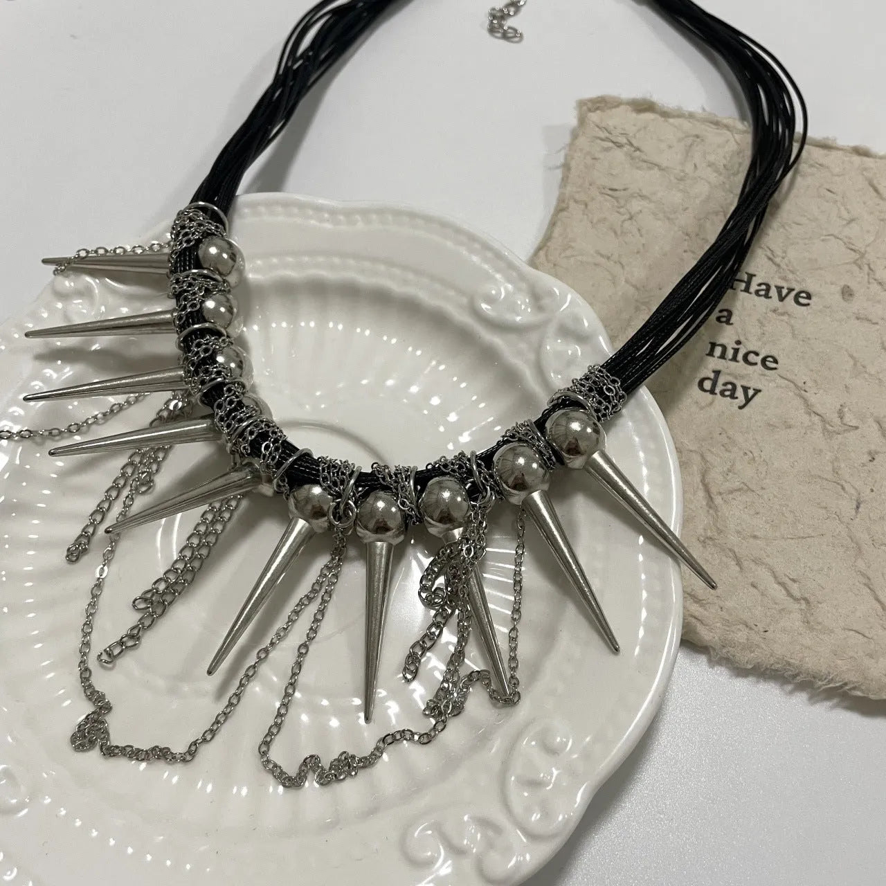 Leather necklace with winding round beads, rivet details, and a long tassel pendant in a metallic colour.