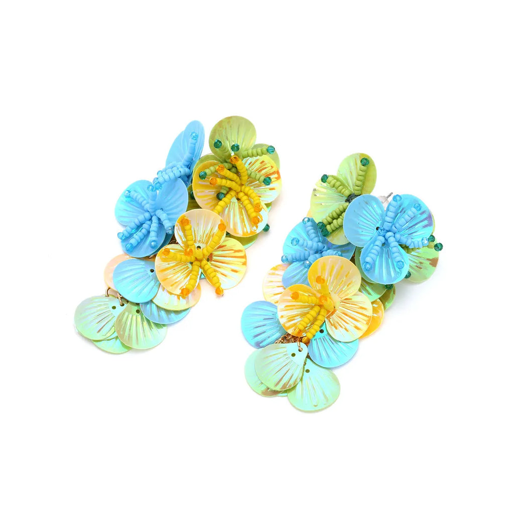 Close-up of handmade purple and green bead flower earrings with leaf details on a white background.