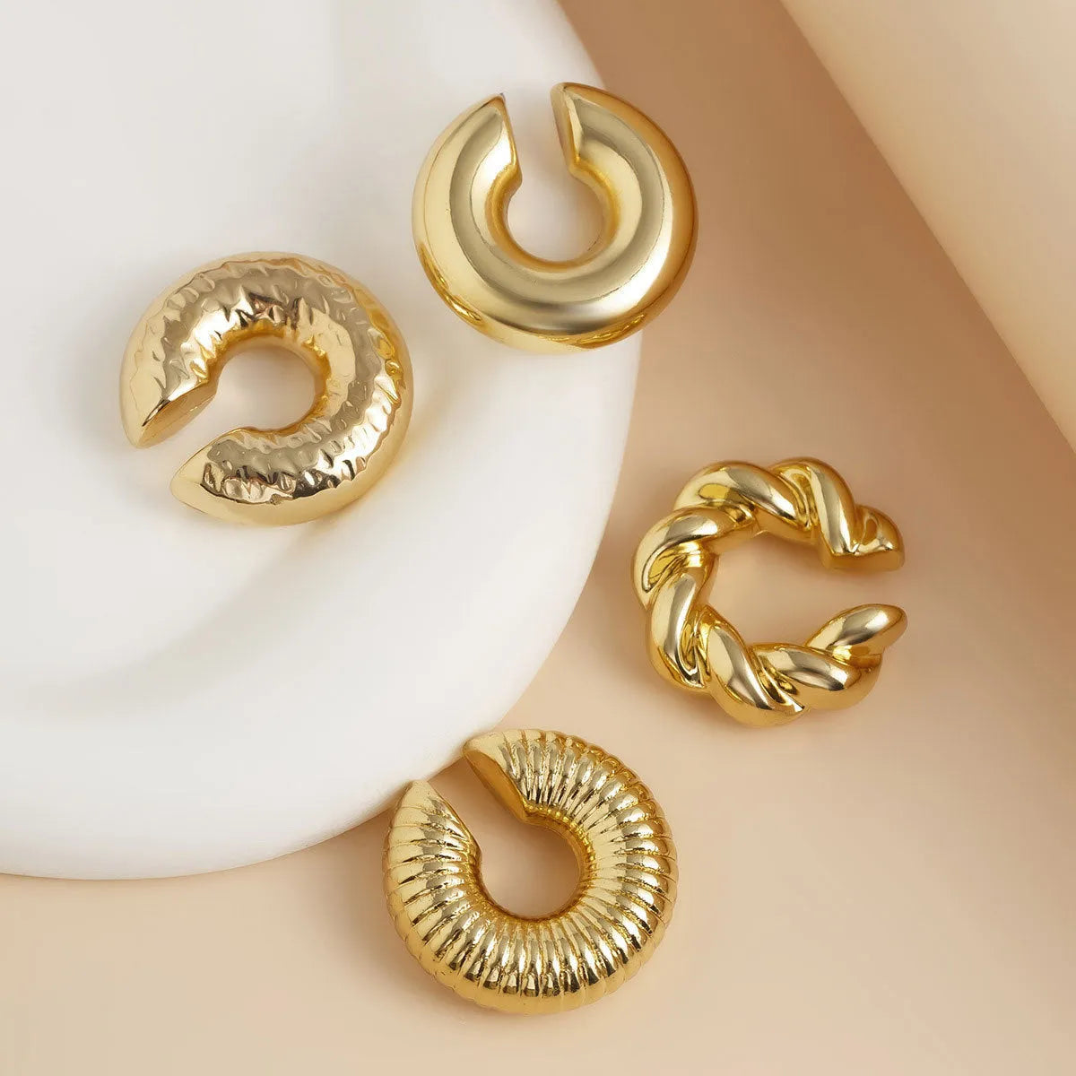 Set of four geometric clip-on earrings for women in gold and silver colours on a plain background