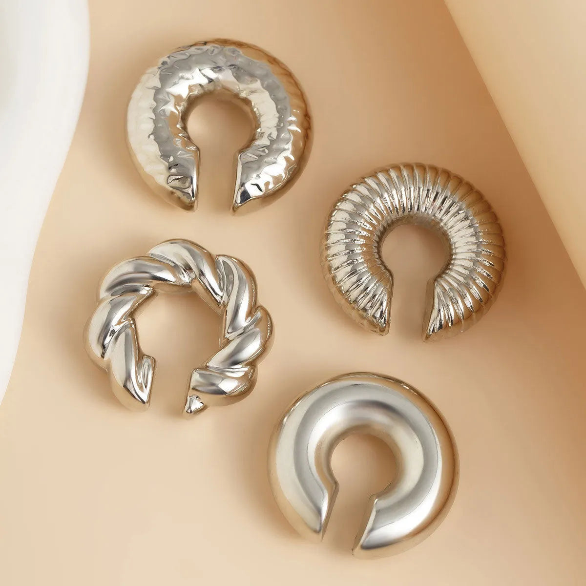 Set of four geometric clip-on earrings for women in gold and silver colours on a plain background