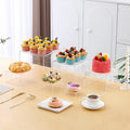 Six white plastic cube dessert display stands arranged on a table.