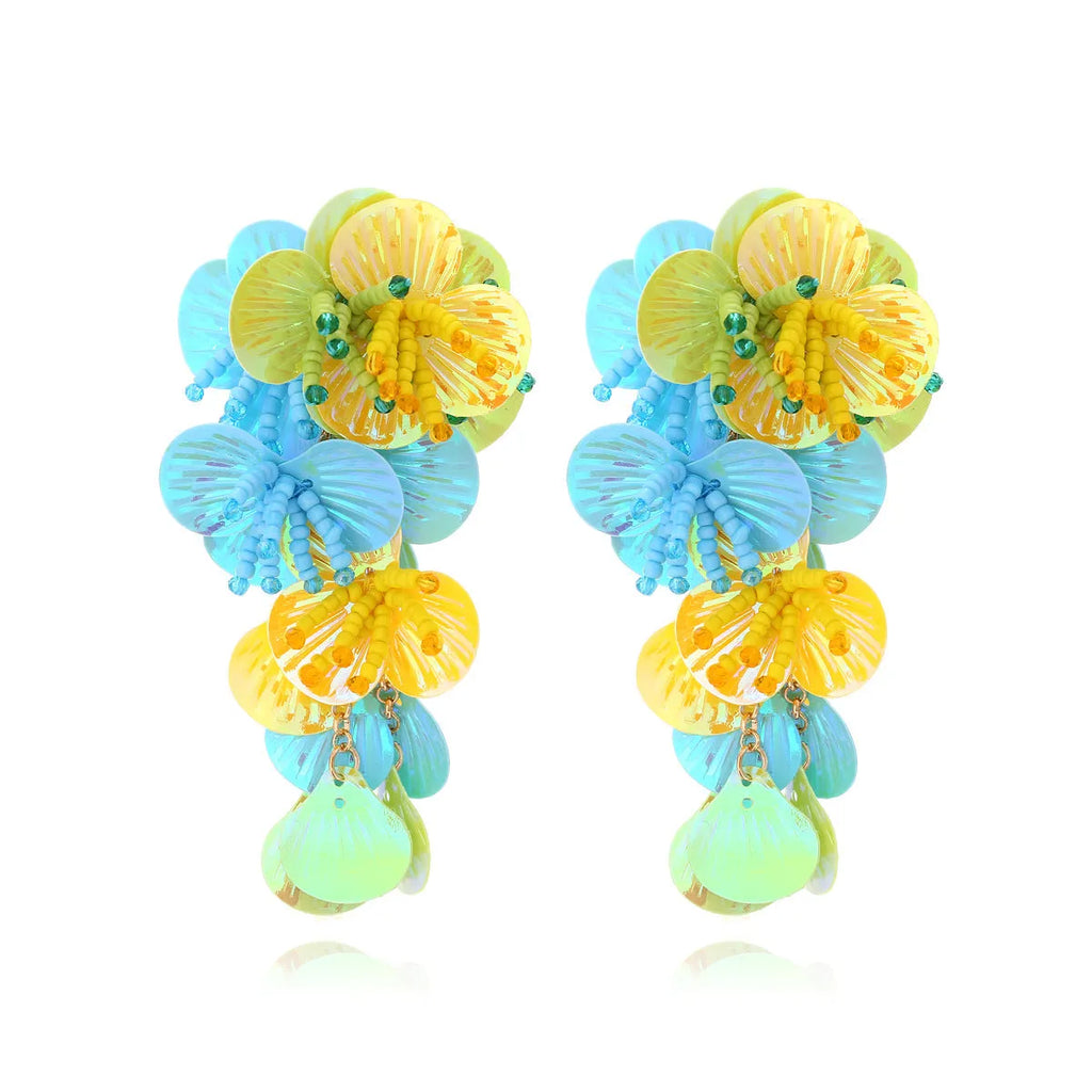 Close-up of handmade purple and green bead flower earrings with leaf details on a white background.