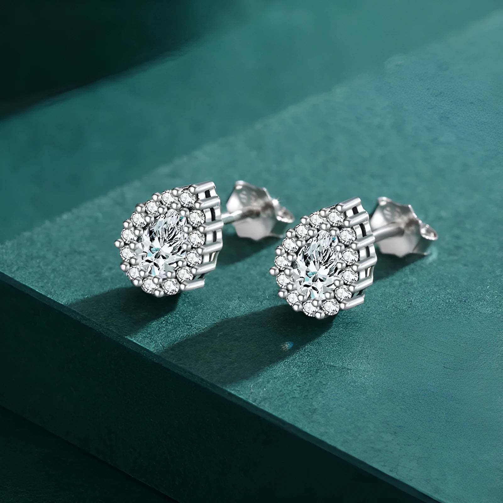 A pair of women's silver water drop shaped stud earrings on a plain background