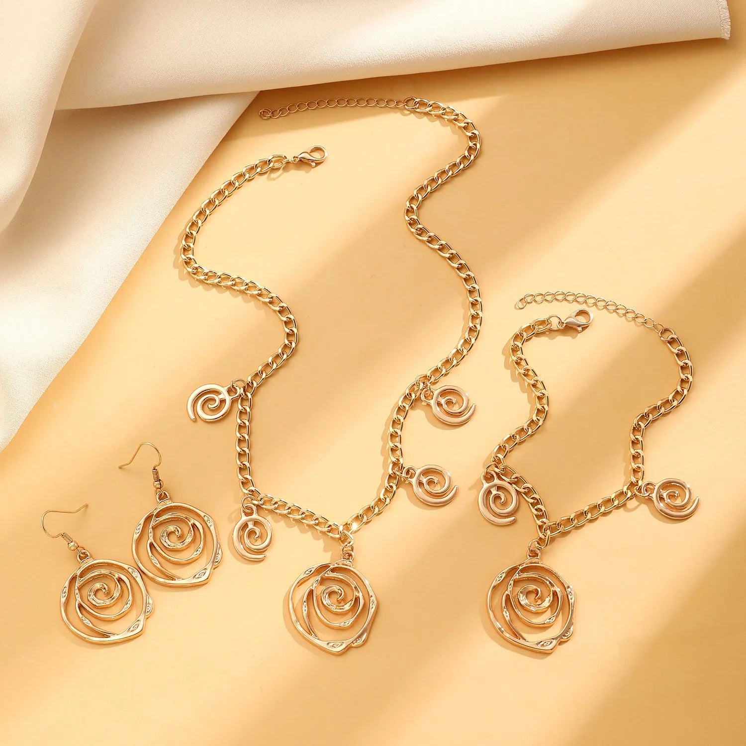 Spiral donut design women's jewellery set showing matching necklace, bracelet, and ear hooks in gold electroplated finish