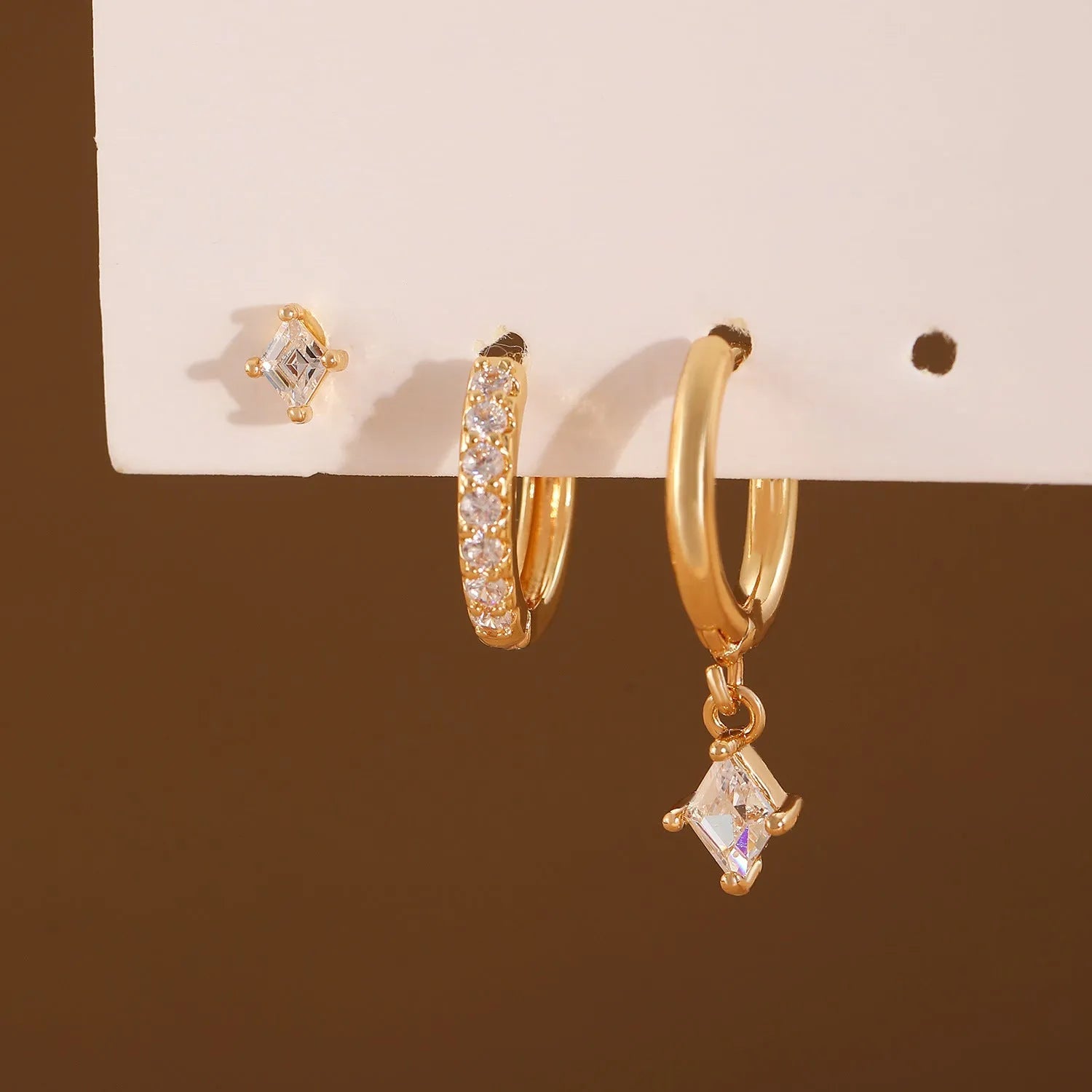 Ladies three-piece earring set with geometric zircon designs in gold and white colours showing pendant, stud, and clip styles