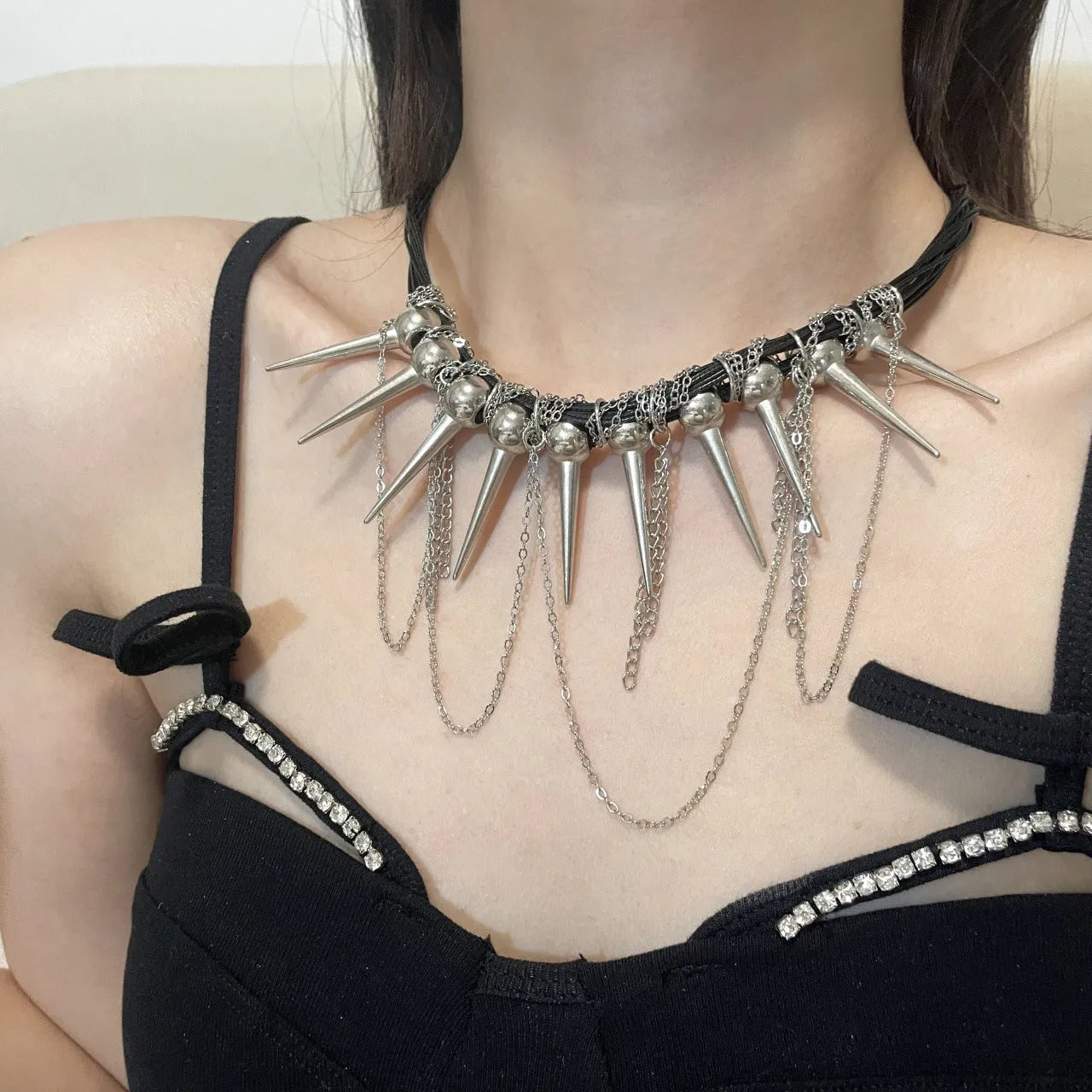 Leather necklace with winding round beads, rivet details, and a long tassel pendant in a metallic colour.