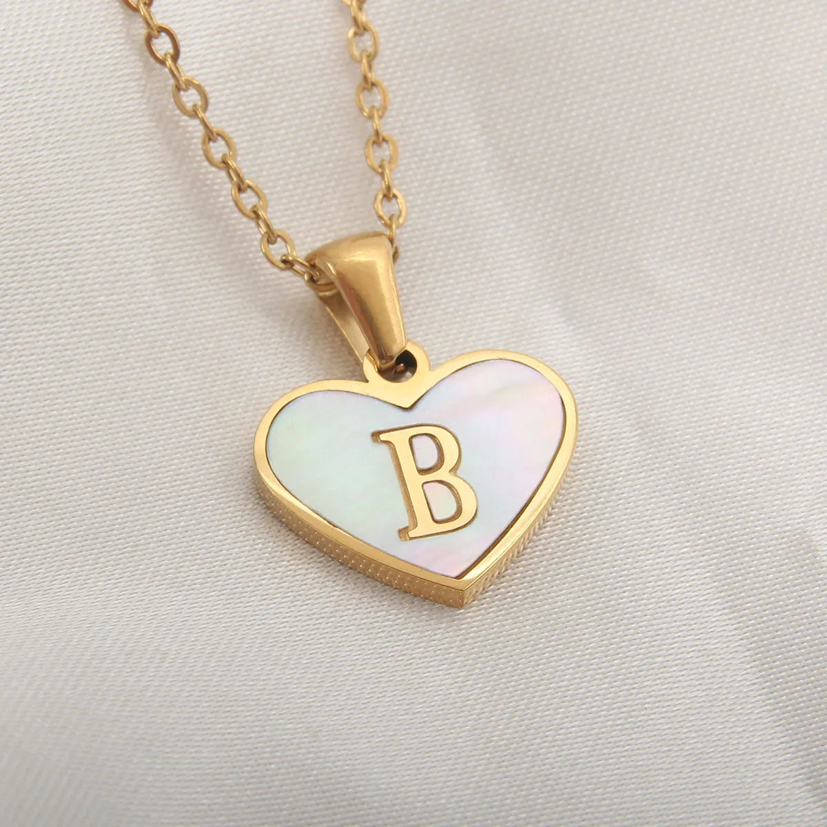 Gold-plated heart necklace with white shell pendant showing initial engraving on stainless steel chain