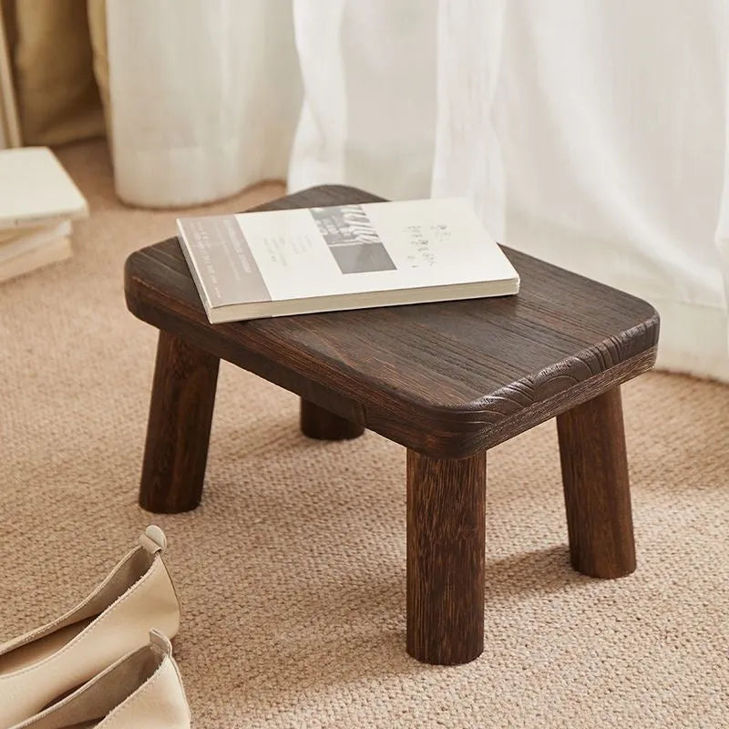 Solid wooden shoe changing stool with a distressed finish, shown in a living room setting.