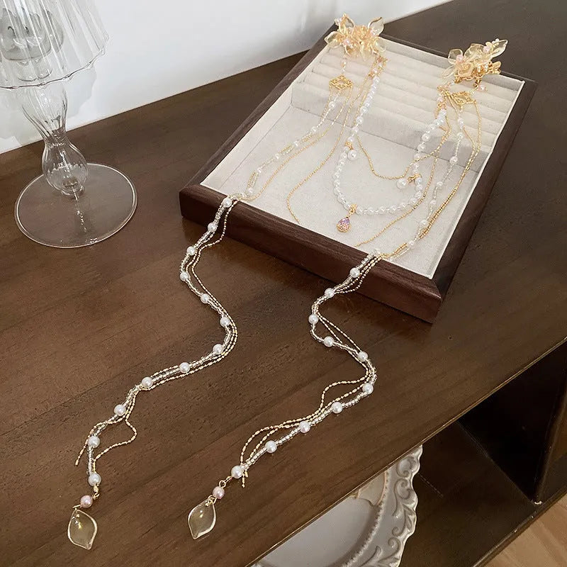 Close-up of a women's floral hairpin with white pearl, clear diamond accents, and a long gold tassel.