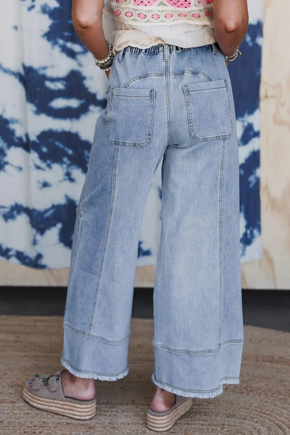 Beau blue wide-leg women's denim trousers with an elasticated drawstring waist and raw hem seam detail laid flat.