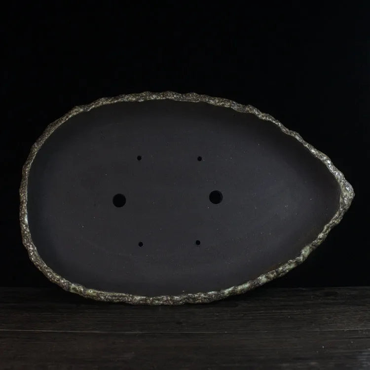 Handmade purple clay flower pot in a unique shape on a floor, showing colour and texture detail.