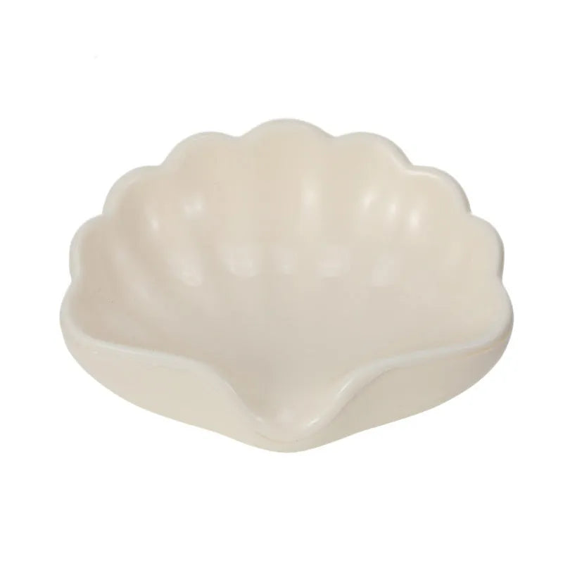 White or pink plastic shell-shaped soap dish with raised design on a bathroom counter.