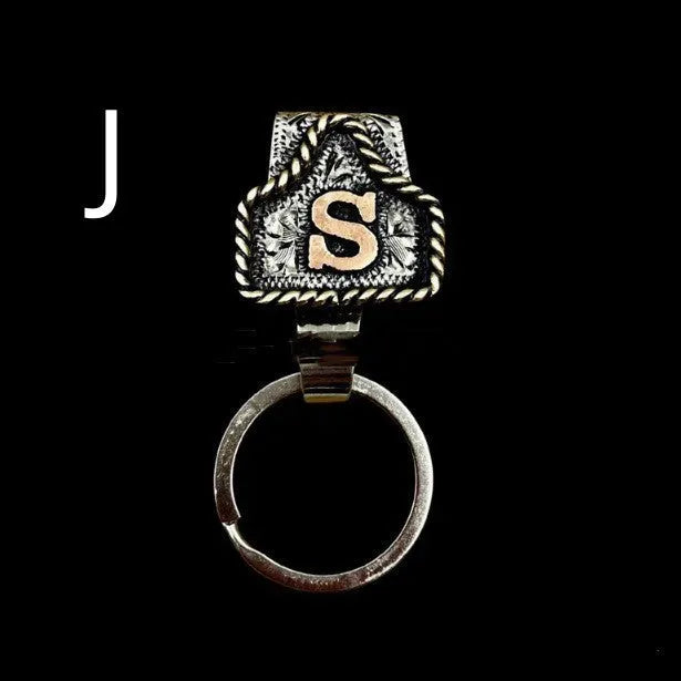 Handmade metal cow tag belt keychain showing one of 26 colour options, each marked with a different alphabet letter.