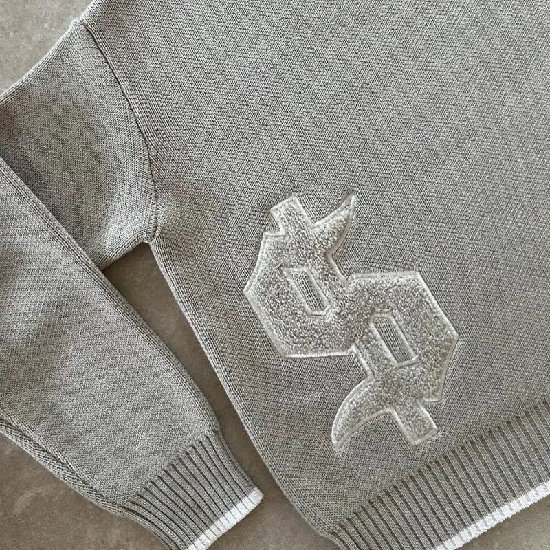 Grey loose-fitting jacquard knit coat on a hanger, showing long sleeves and textured knit pattern.