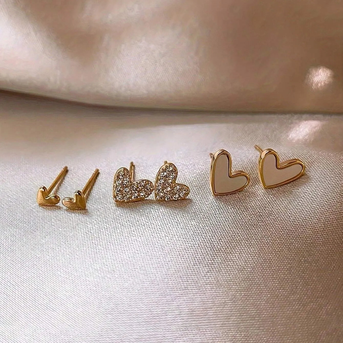 Three pairs of heart-shaped alloy earrings with electroplated finish in gold, black, and pink colours