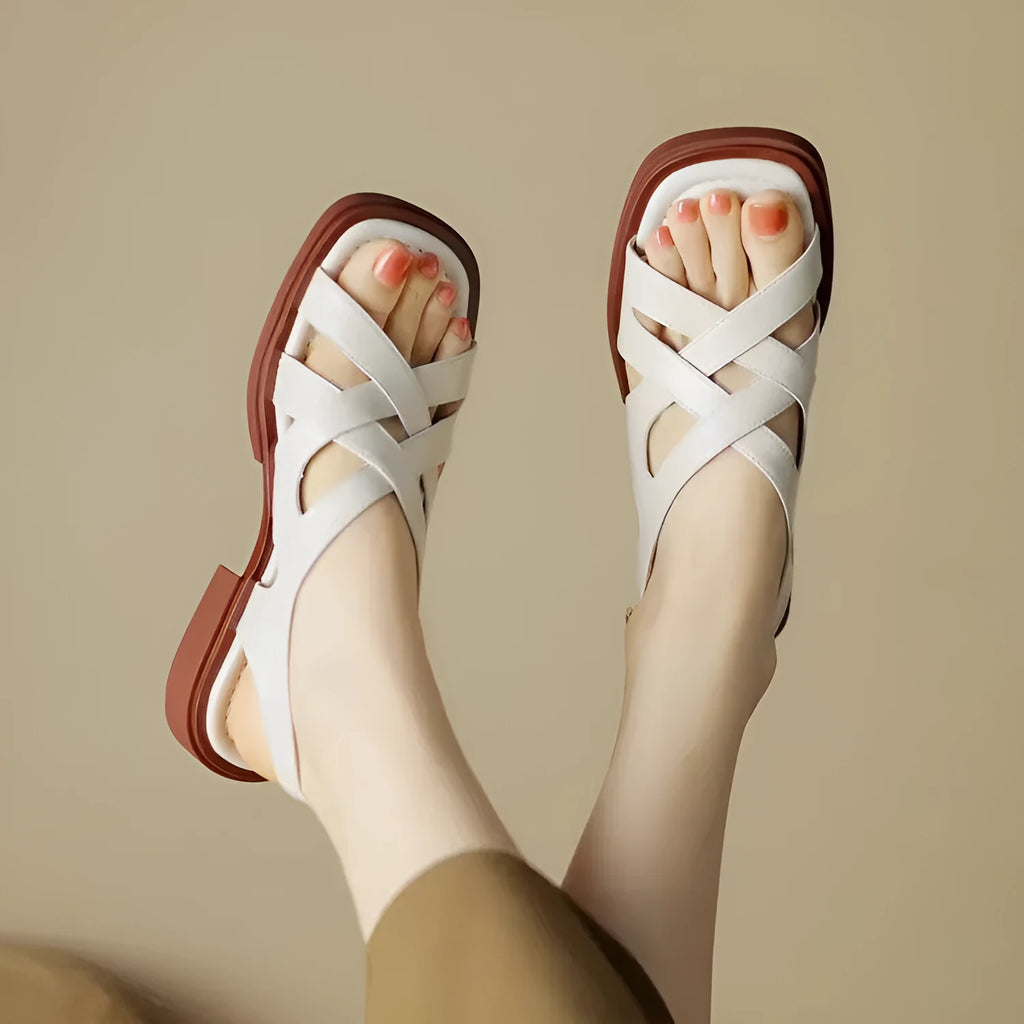 Women's black patent leather square toe sandals with cross strap on a white background.
