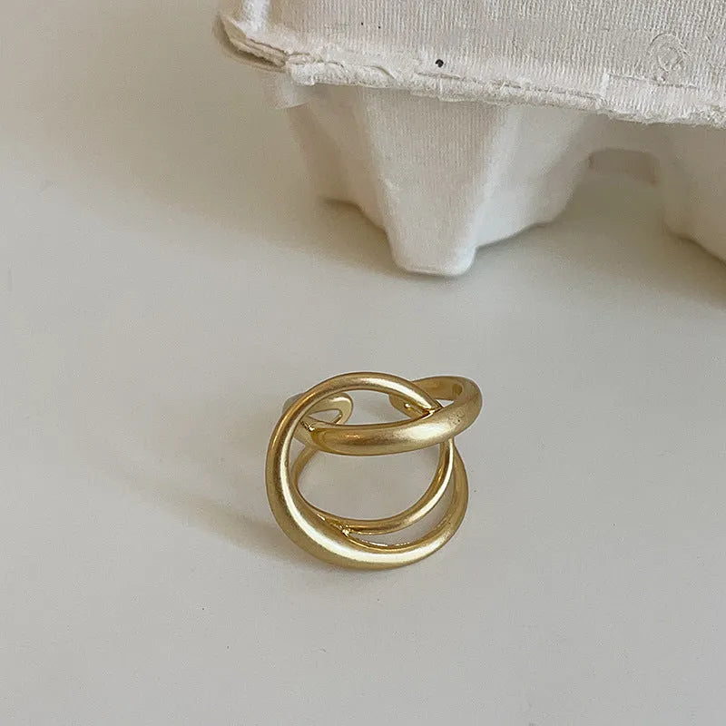 Geometric open ring for women with 3D interlaced matte metal design, shown in gold plating.