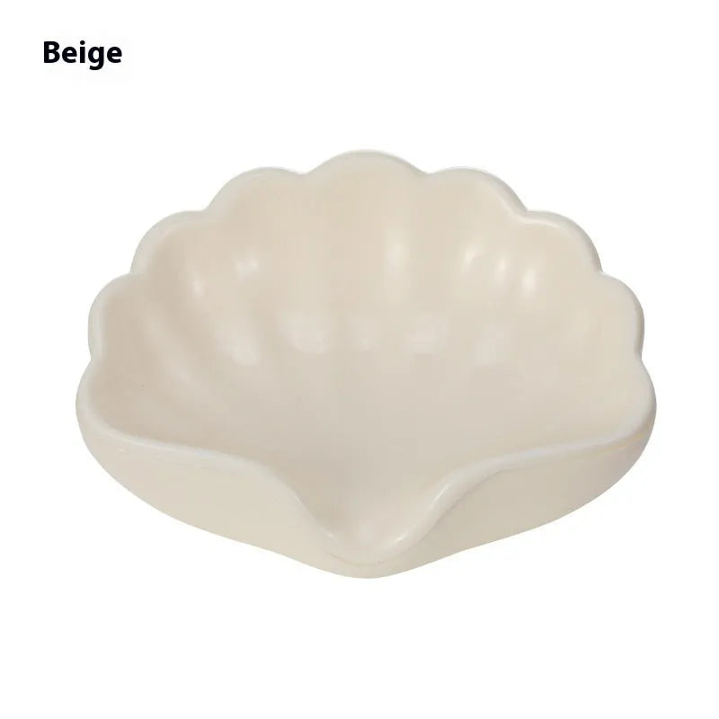 White or pink plastic shell-shaped soap dish with raised design on a bathroom counter.