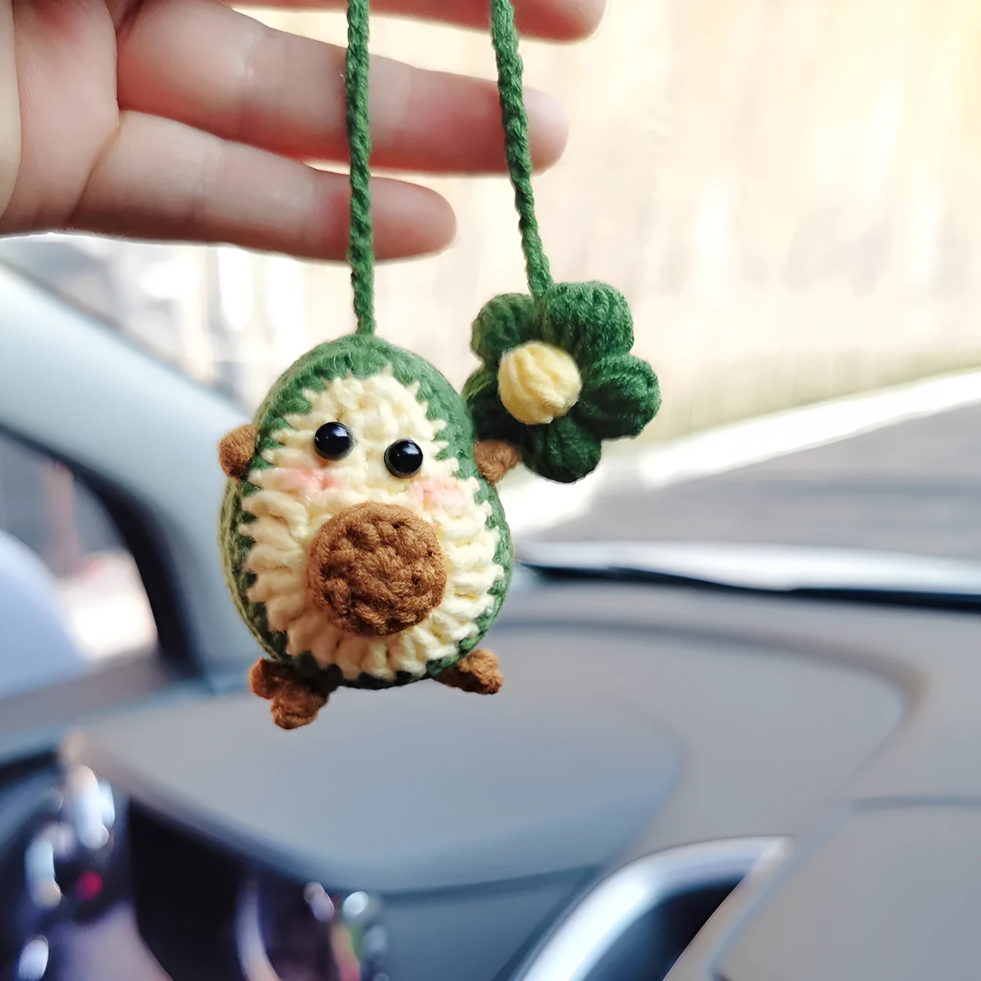 Handmade crocheted avocado-shaped car pendant with a rainbow flower on a green background.