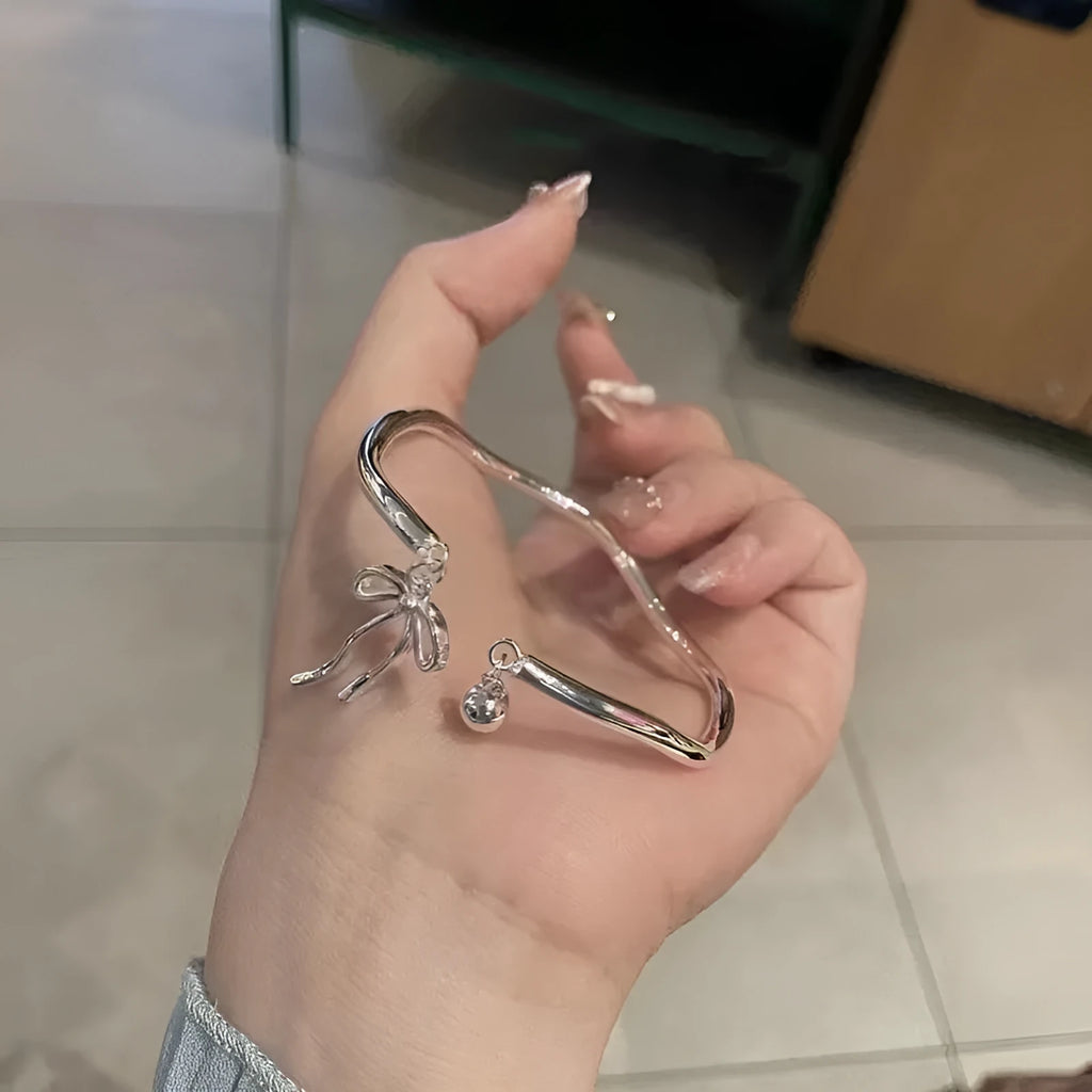 Silver adjustable bracelet with bow detail and bell opening clasp on wrist