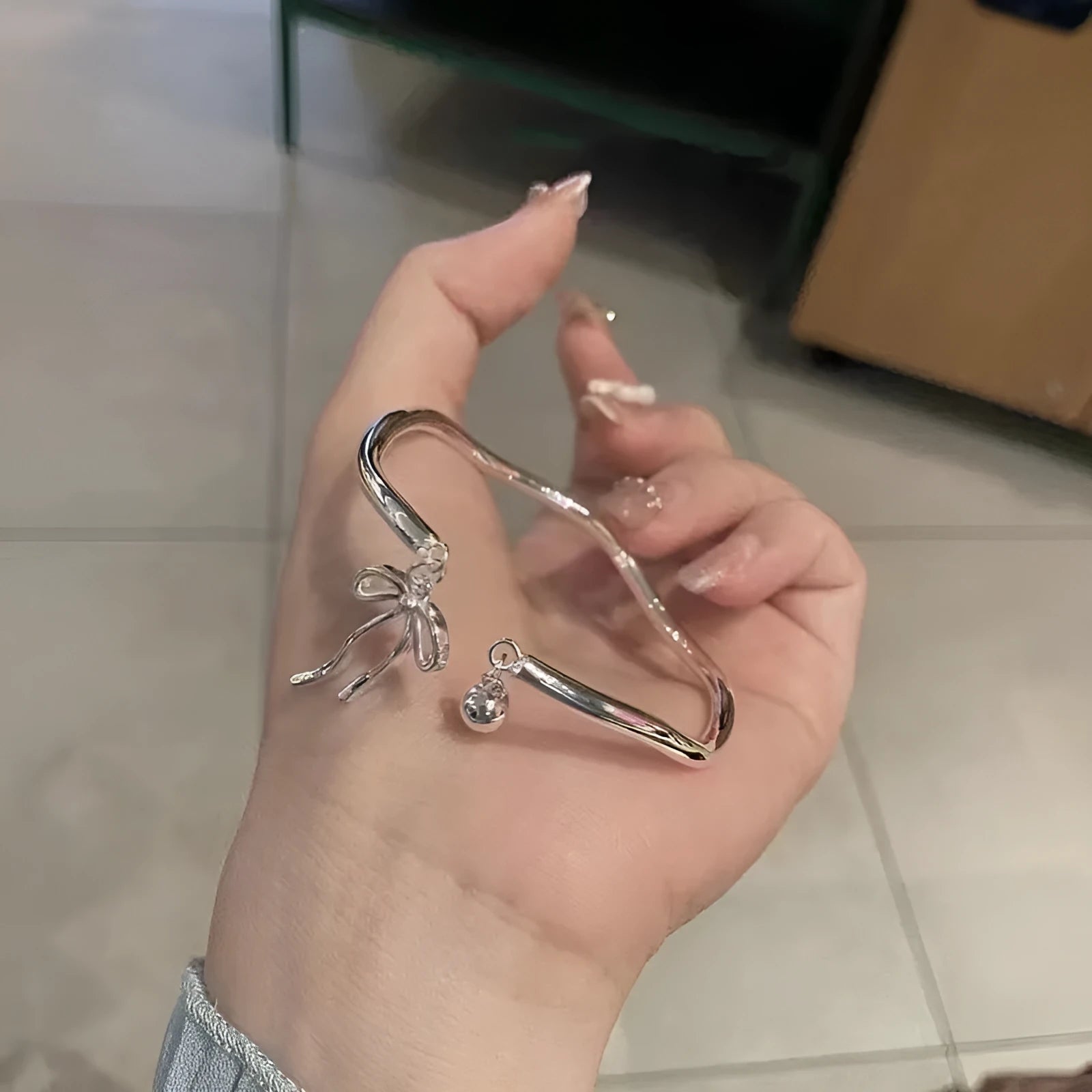Silver adjustable bracelet with bow detail and bell opening clasp on wrist