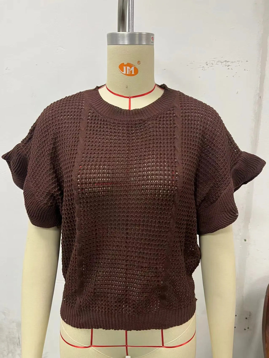 Knitted loose pullover sweater with ruffled short sleeves and a 3D twisted string pattern, shown in a neutral colour.