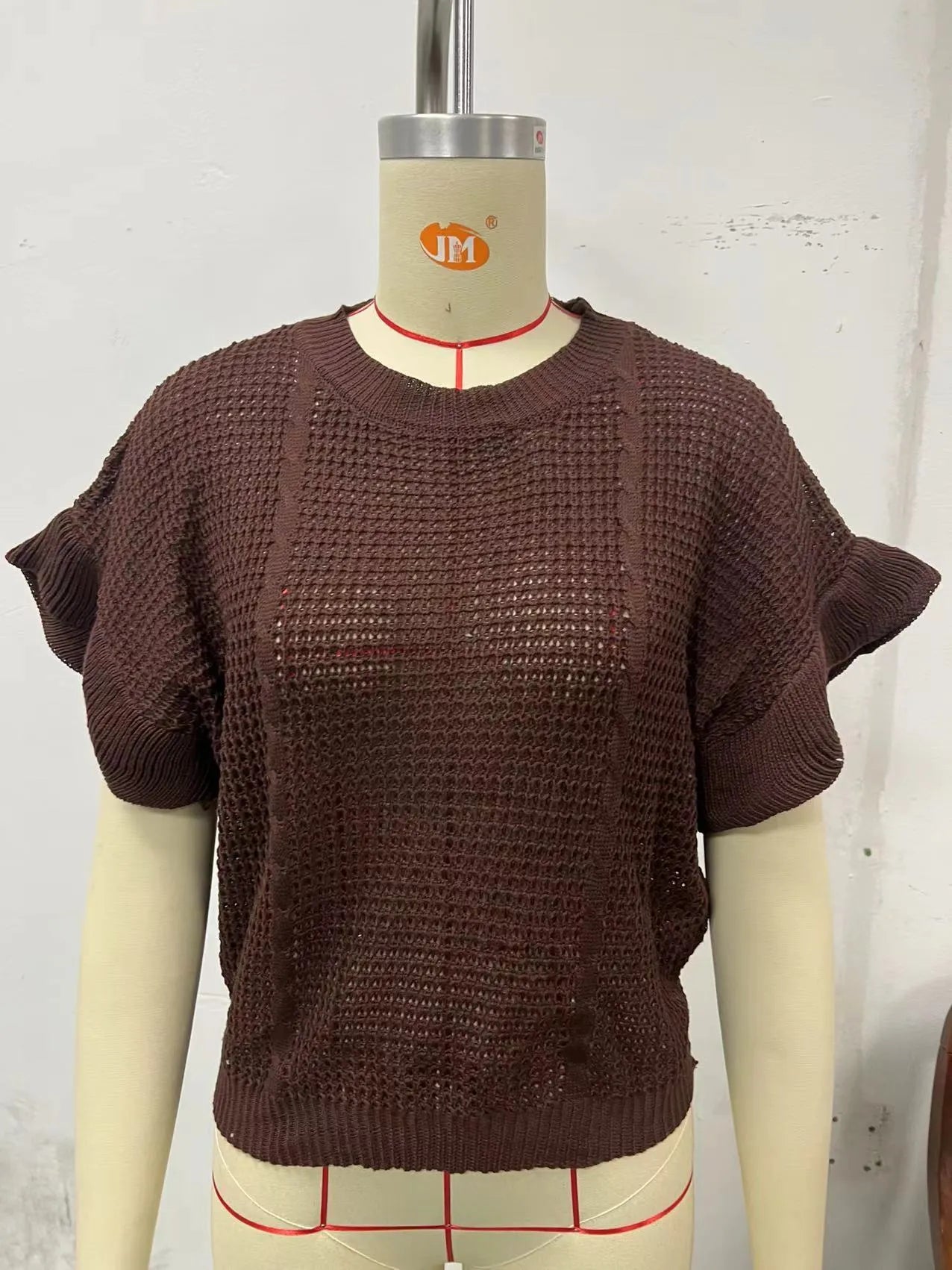 Knitted loose pullover sweater with ruffled short sleeves and a 3D twisted string pattern, shown in a neutral colour.
