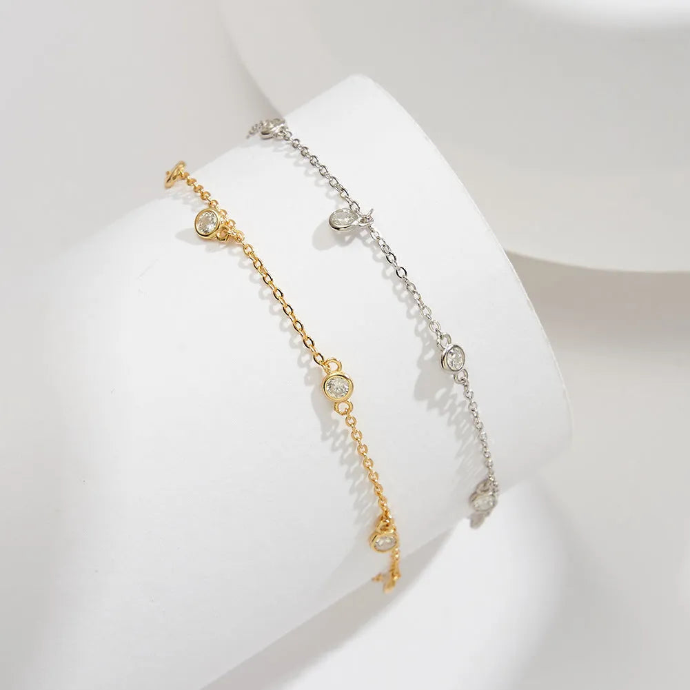 Close-up of a women's silver anklet with a geometric zirconium pendant on a simple chain.
