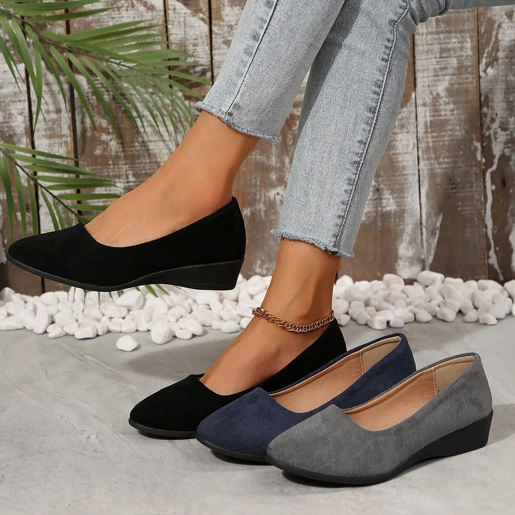 Women's black suede wedge pumps with pointed toe and low rubber sole on a light background