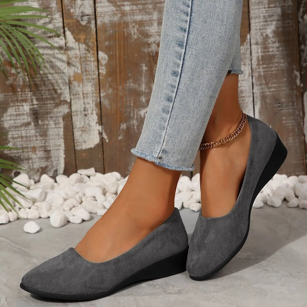 Women's black suede wedge pumps with pointed toe and low rubber sole on a light background