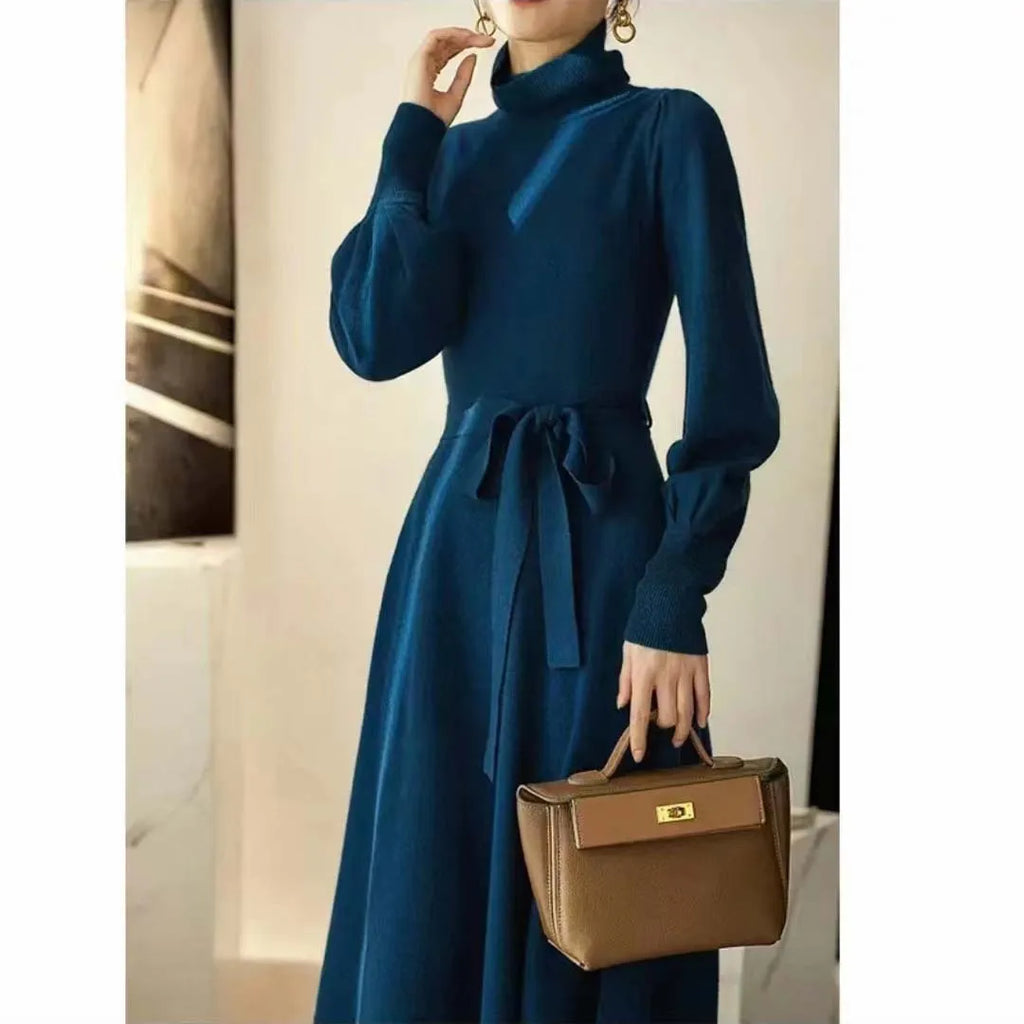 A woman wearing a rose red turtleneck knit dress with long sleeves, an elastic waist, and a loose mid-length hem.