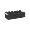 A minimalist woven paper storage basket in khaki colour on a wooden table, holding remote controls and pens.