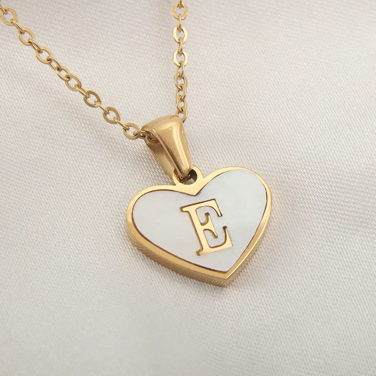 Gold-plated heart necklace with white shell pendant showing initial engraving on stainless steel chain