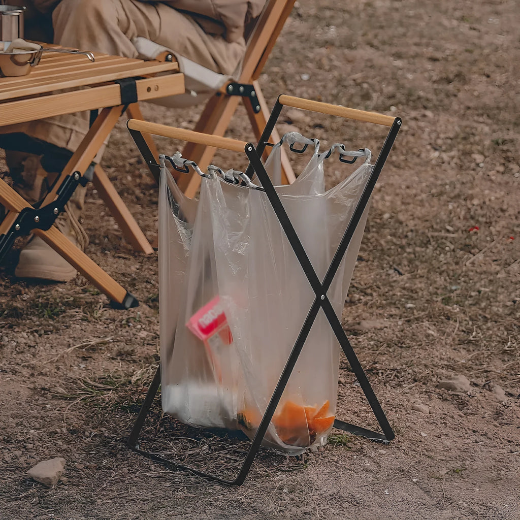 Black folding outdoor trash rack with wooden handle standing on a patio.