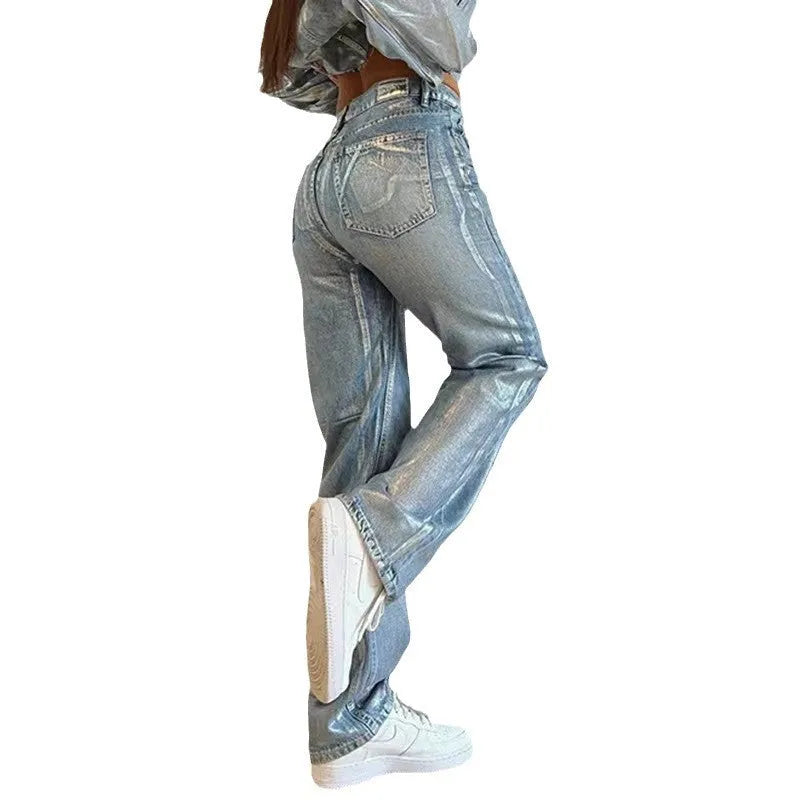 Women's washed blue high-waist straight-leg jeans with silver contrast hardware on a denim background.