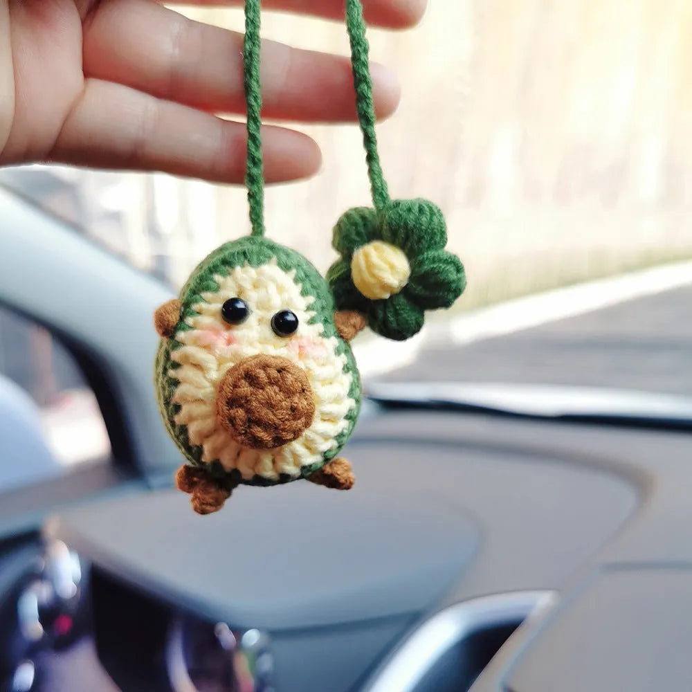 Handmade crocheted avocado-shaped car pendant with a rainbow flower on a green background.