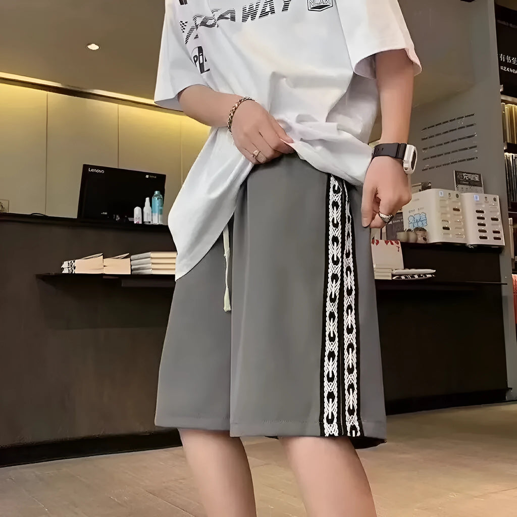 Men's black loose-fit polyester track pants with an elasticated waist, shown in a casual setting.