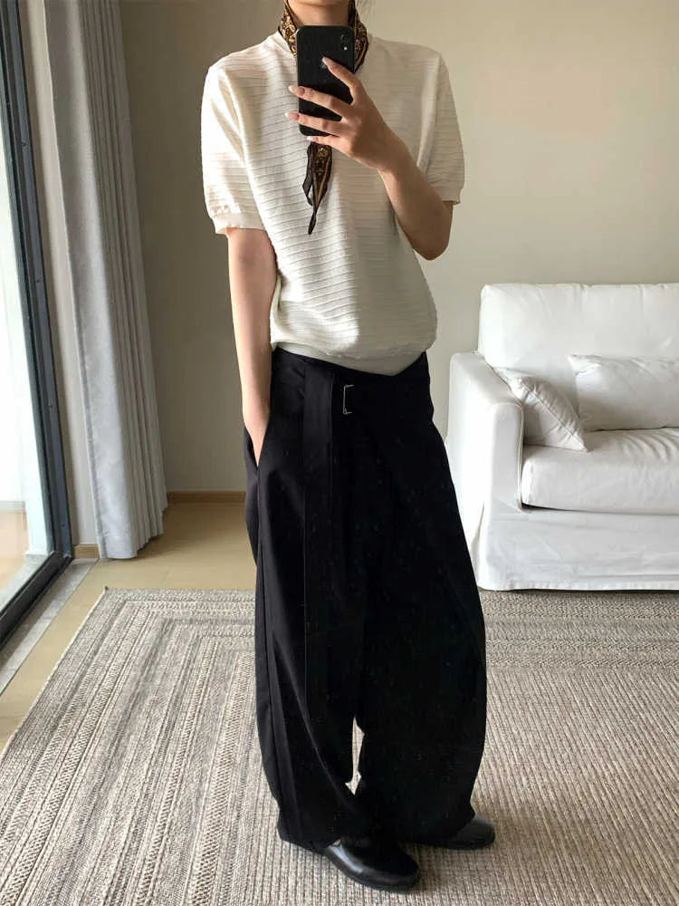 Black loose fit straight leg trousers with a single pleat and adjustable waistband on a hanger.