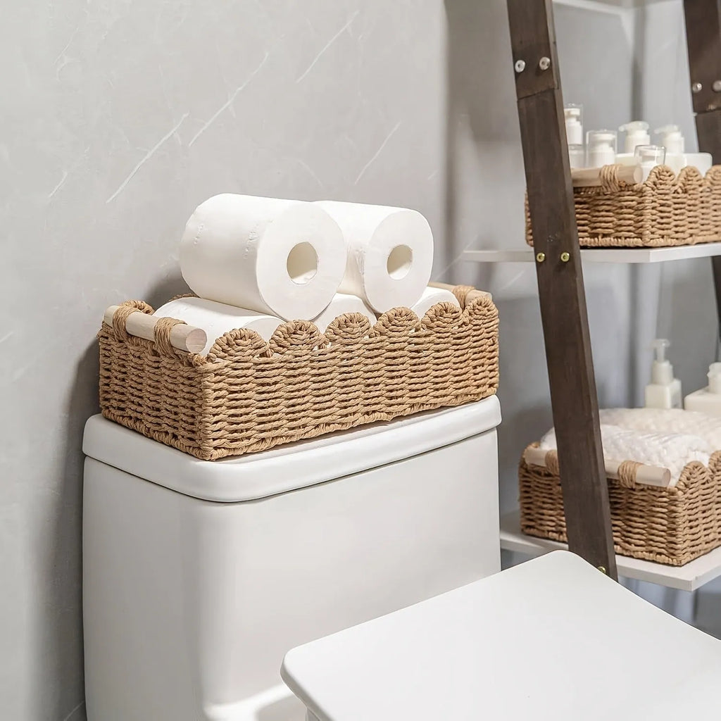 A minimalist woven paper storage basket in khaki colour on a wooden table, holding remote controls and pens.