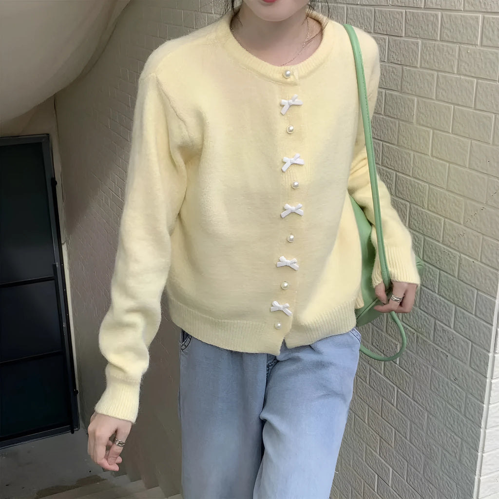 Women's light blue acrylic cardigan sweater with pearl buttons and a decorative bow detail.