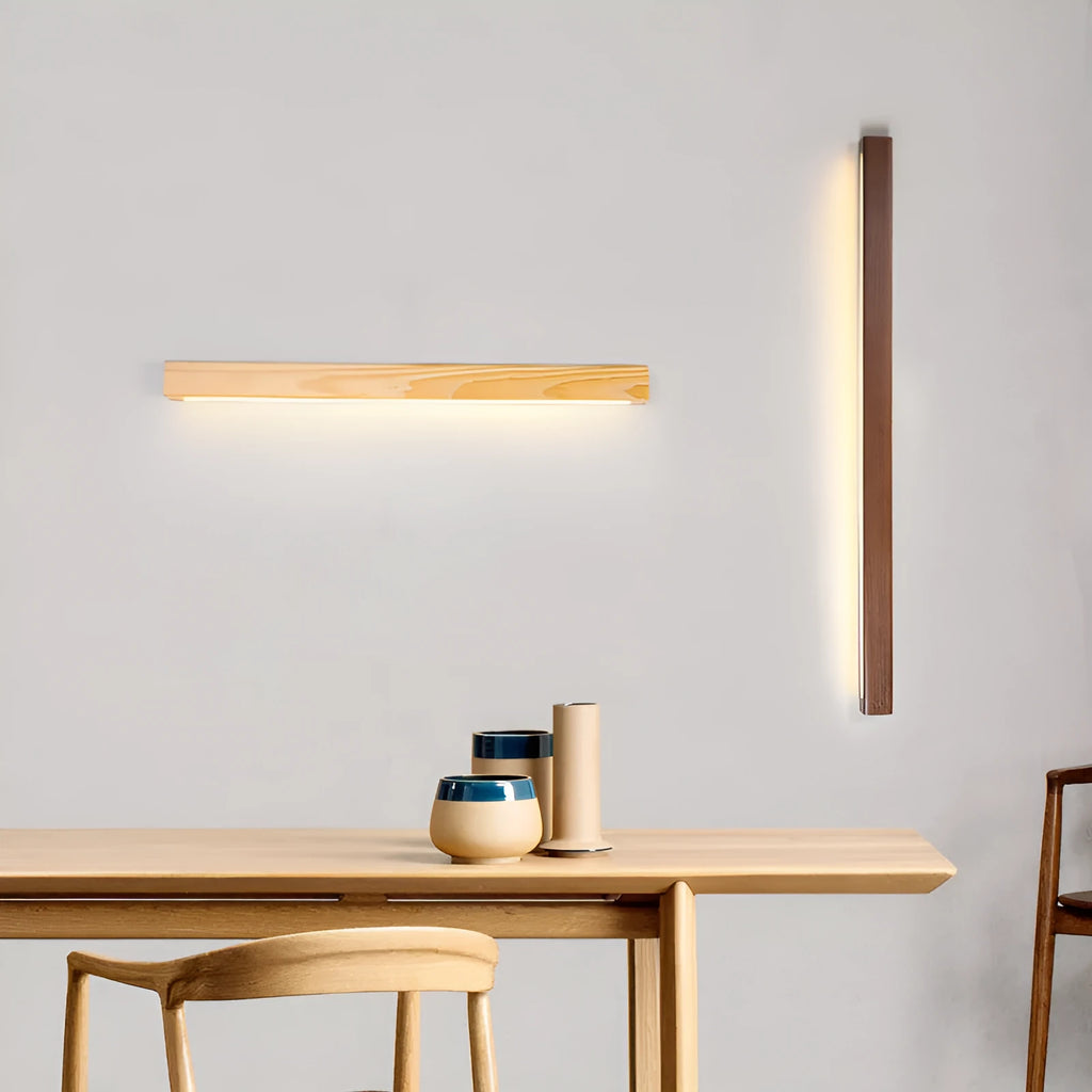 Modern walnut-coloured wood and acrylic log strip wall lamp in three lengths on a white wall.