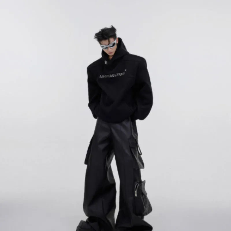 Man wearing a loose black hooded sweater with metallic 3D printed design and structured shoulder pads.